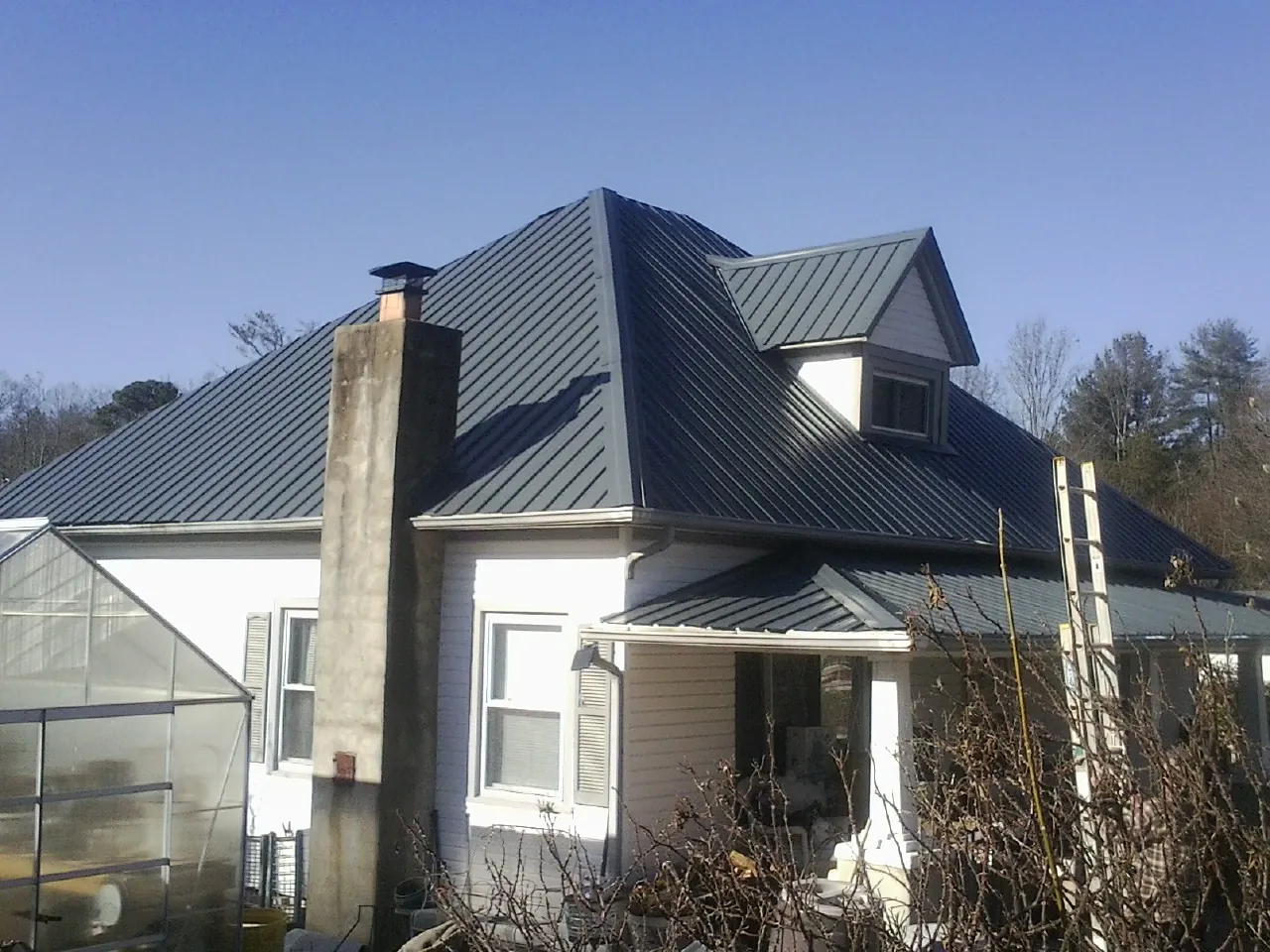 Dark blue standing seam metal roof on a white farmhouse with dormer — Slate & Tile Roof Repair by Roofing Brothers in Curtis