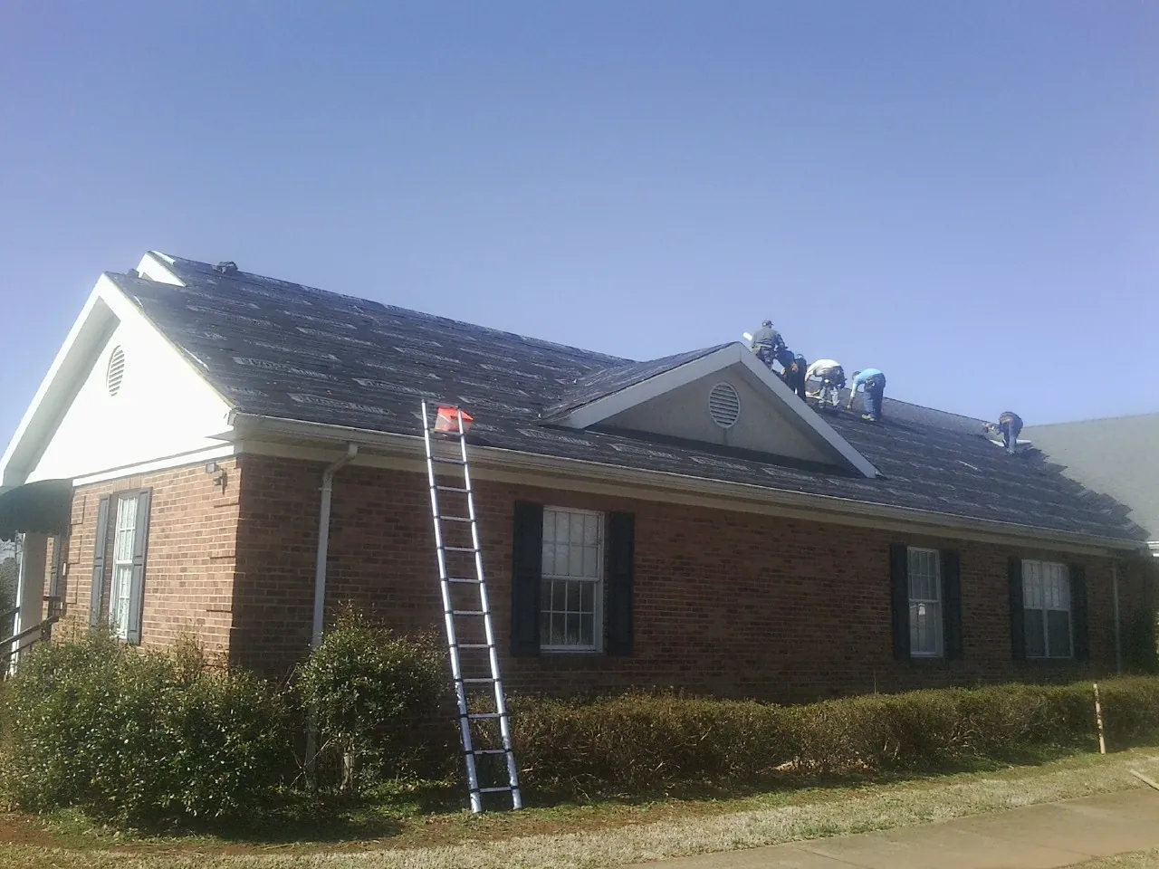 Crew tearing shingles off a brick ranch roof with a ladder set — Emergency Roof Repair work by our crew in Curtis