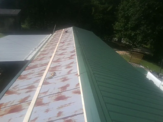 Old rusted panels beside newly installed green metal roofing — Wind Damage Roof Repair by Roofing Brothers in Curtis