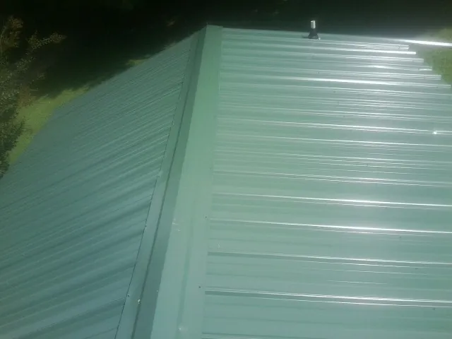 New green metal panels meeting at the ridge of a roof — Flat Roof Repair work by our crew in Curtis