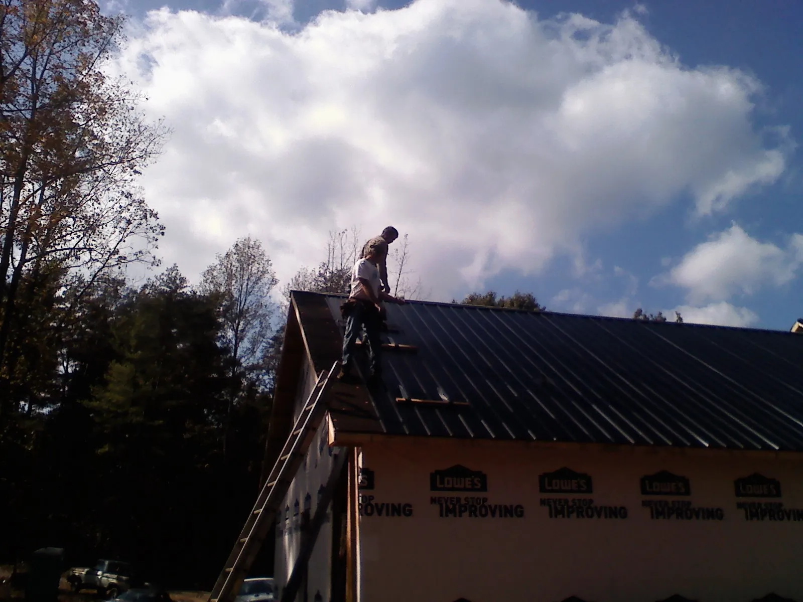Roofer fastening dark metal panels high against a cloudy sky, from a Roof Inspection job in Curtis